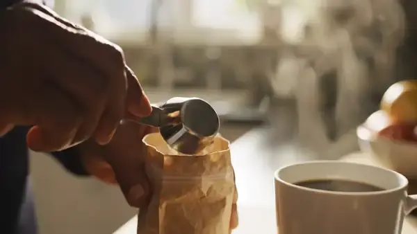 A man's hands leveling a small scoop of powder and tipping it into a mug of coffee